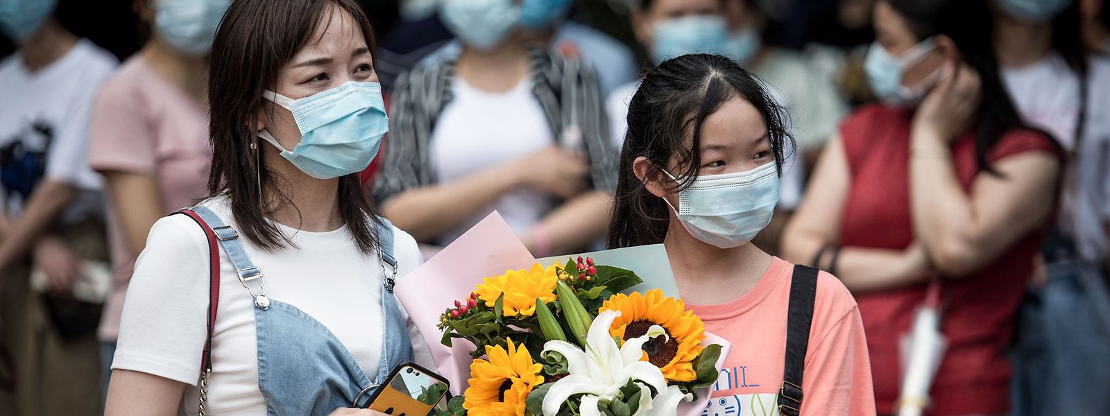 Mit einem Blumenstrauß warten zwei Mädchen auf eine Schülerin bei der Abschlussprüfung.