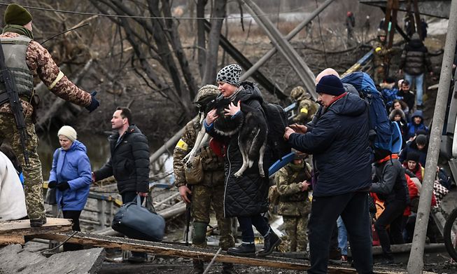 People cross a destroyed bridge as they evacuate the city of Irpin, northwest of Kyiv, on Saturday