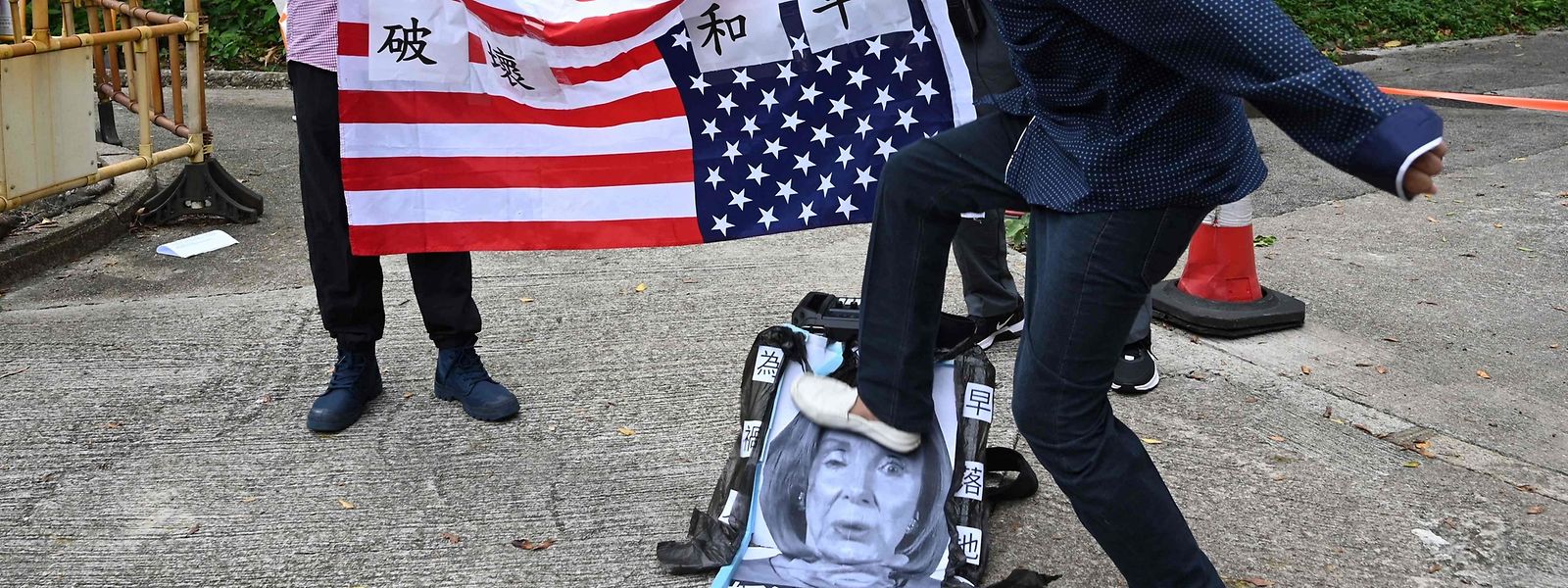 Um protestante pró-Pequim pontapeia um cartaz com o retrato de Nancy Pelosi, num protesto em frente ao consulado americano em Hong Kong.