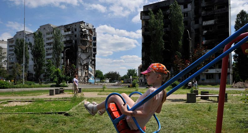 TOPSHOT - A girl rides a swing on a playground in front of a destroyed residential building in the town of Borodyanka on June 7, 2022, amid the Russian invasion of Ukraine. (Photo by Sergei CHUZAVKOV / AFP)