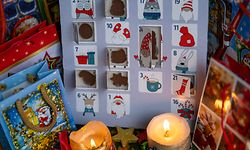 Ein mit Schokolade gefüllter Adventskalender steht neben zwei Kerzen und Geschenktüten auf einem Tisch. 