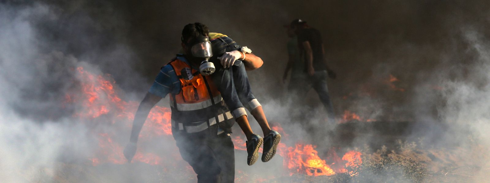 Ein Sanitäter mit Gasmaske trägt einen verletzten palästinensichen Jungen aus der Gefahrenzone.