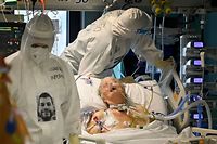 Medical workers of the COVID-19 intensive care unit (ICU) at the Santo Stefano hospital in Prato, near Florence, Tuscany, wearing their PPE (personal protective equipment) with photos of themselves printed and their name written on it, are pictured while tending to a patient on December 17, 2020 at the hospital in Prato. - Doctors and nurses in the ICU of Santo Stefano hospital wear protective gear with their real face pictured on it  to be recognized by patients and reassure them. (Photo by Alberto PIZZOLI / AFP)