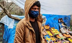 A migrant wearing a facemask for protective measures walks by a fruit and vegetable stall at a makeshift camp next to the Moria camp on the Greek island of Lesbos on April 2, 2020. - Over 20 coronavirus cases were found in a camp near Athens this week. At the camp of Moria on the island of Lesbos, both doctors and migrants say health precautions are not much help in a facility that is so badly overcrowded. The novel coronavirus could spread faster in overcrowded refugee and displaced persons camps than it has anywhere else so far, warned the International rescue Committee. (Photo by Manolis LAGOUTARIS / AFP)