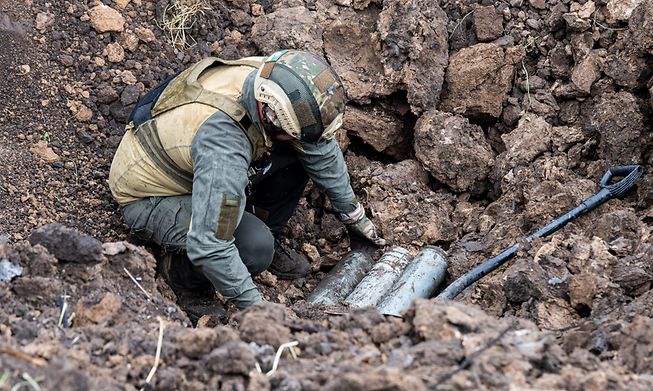 A soldier sits in a pit where unexploded, suspected Russian ammunition, was placed by a group of the Ukrainian National Guard