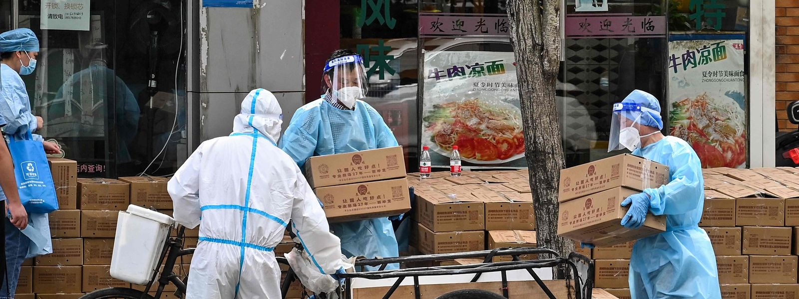 In einem Viertel von Shanghai verteilen Helfer in Schutzkleidung Lebensmittelpakete.