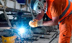 Ein Bauarbeiter schweißt auf einer Baustelle an einer Baumaschine. 