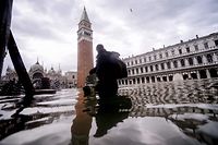 A general view shows a person walking across the flooded St. Mark's Square, with St. Mark's Basilica (Rear L) and the Bell Tower on November 15, 2019 in Venice, two days after the city suffered its highest tide in 50 years. - Flood-hit Venice was bracing for another exceptional high tide on November 15, as Italy declared a state of emergency for the UNESCO city where perilous deluges have caused millions of euros worth of damage. (Photo by Filippo MONTEFORTE / AFP)