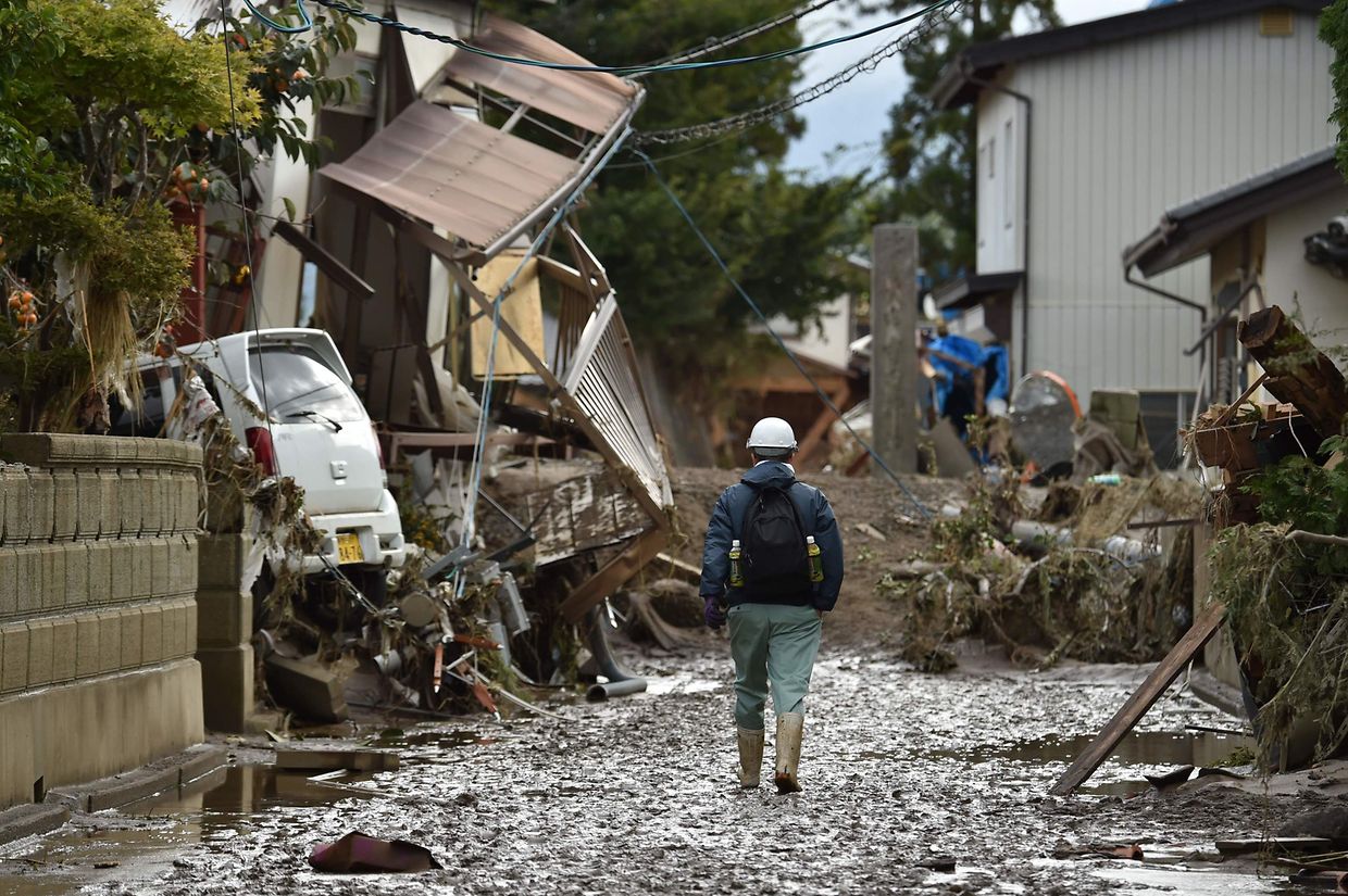 A man walks past damaged homes and debris littering the area near where a river burst its banks in Nagano on October 15, 2019, after Typhoon Hagibis hit Japan on October 12 unleashing high winds, torrential rain and triggered landslides and catastrophic flooding. - Rescuers in Japan worked into a third day on October 15 in an increasingly desperate search for survivors of a powerful typhoon that killed nearly 70 people and caused widespread destruction. (Photo by Kazuhiro NOGI / AFP)