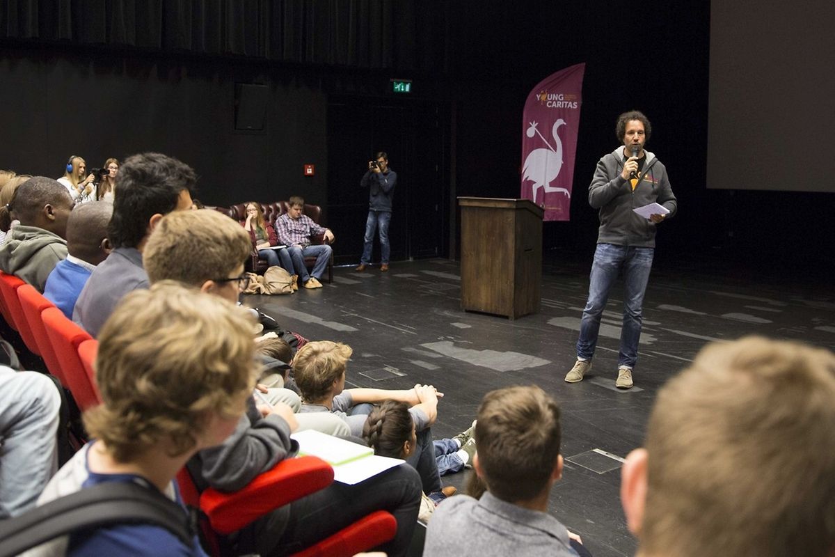 Flüchtlinge und Schüler sitzen nebeneinander in den Reihen und hören dem Sprecher gebannt zu.