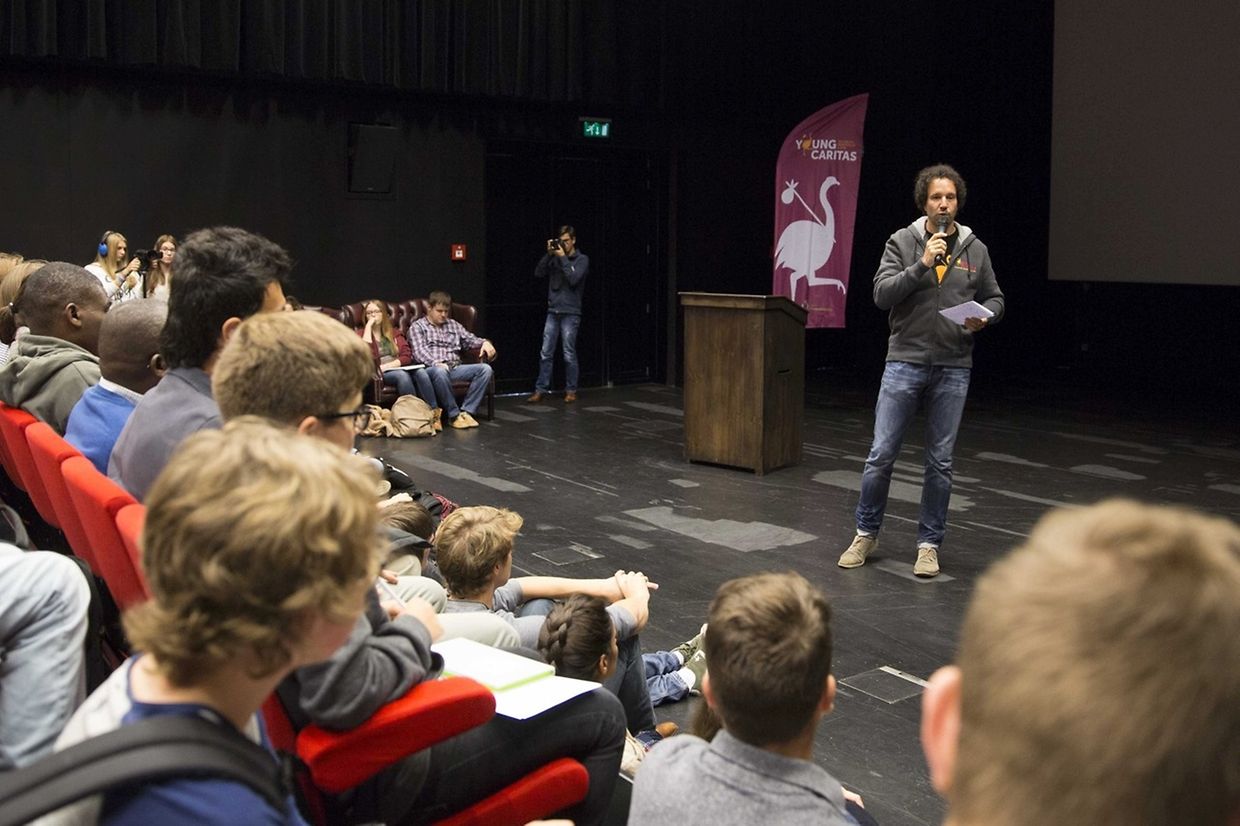 Flüchtlinge und Schüler sitzen nebeneinander in den Reihen und hören dem Sprecher gebannt zu.