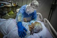 Trabalhador da saúde presta apoio a uma idosa hospitalizada com covid-19, em Portugal. Imagem foi eleita uma das fotos do ano pela agência France-Presse.