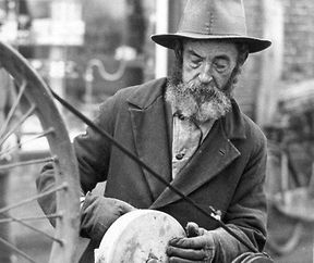 Een scharensliep aan het werk. Hij houdt de slijpsteen vast, die door een fietswiel dmv een snaar wordt aangedreven. [1931].