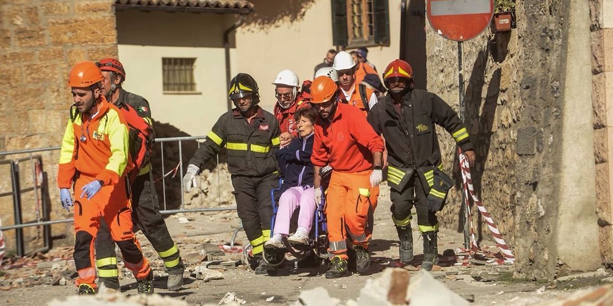 Rettungshelfer tragen eine Frau in ihrem Rollstuhl aus den Trümmern.