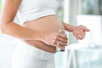 Midsection of pregnant woman with pills and water at home - Bilder 