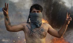 20.01.2020, Irak, Baghdad: Bei Zusammenstößen zwischen Sicherheitskräften und regierungskritischen Demonstranten lässt steht ein Demonstrant vor brennenden Reifen und zeigt das Victory-Zeichen. Foto: Ameer Al Mohammedaw/dpa +++ dpa-Bildfunk +++