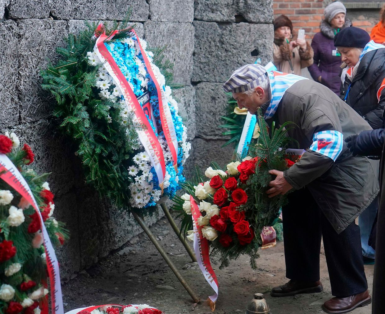 Ein Holocaust-Überlebender legt an der Todeswand in Auschwitz einen Blumenkranz nieder. 