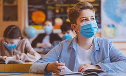 High school students at school, wearing N95 Face masks. Teenage boy sitting at the school desk, looking away and thinking.