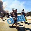 TOPSHOT - People leave the beach with their belongings as a fire burns a forest behind them in Bormes-les-Mimosas, southeastern France, on July 26, 2017.
At least 10,000 people, including thousands of holidaymakers, were evacuated overnight after a new wildfire broke out in southern France, which was already battling massive blazes, authorities said on July 26. / AFP PHOTO / Anne-Christine POUJOULAT