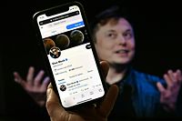 In this photo illustration, a phone screen displays the Twitter account of Elon Musk with a photo of him shown in the background, on April 14, 2022, in Washington, DC. - Tesla chief Elon Musk has launched a hostile takeover bid for Twitter, insisting it was a "best and final offer" and that he was the only person capable of unlocking the full potential of the platform. (Photo by Olivier DOULIERY / AFP)