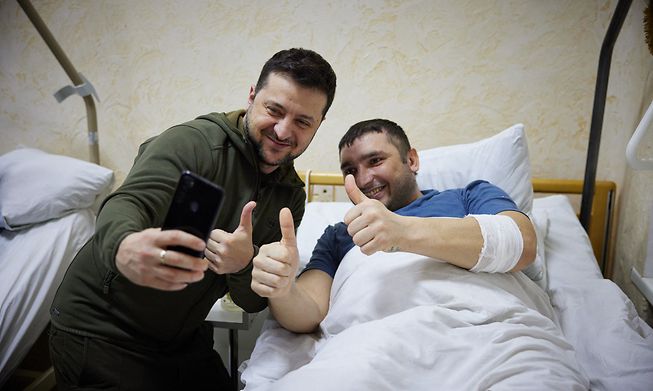 Ukrainian President Volodymyr Zelenskiy (L) snaps a selfie with an injured man laying on a bed during a visit at a military hospital In this handout picture released by the Ukrainian Presidency Press Office on Sunday