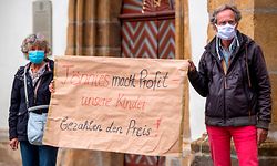 dpatopbilder - 18.06.2020, Nordrhein-Westfalen, Rheda-Wiedenbrück: Demonstranten halten während einer Mahnwache zur Situation beim Fleischwerk Tönnies auf dem Marktplatz in Rheda-Wiedenbrück ein Schild mit der Aufschrift "Tönnies macht Profit - unsere Kinder bezahlen den Preis!". Bei mehr als 600 Mitarbeitern des Fleischkonzerns Tönnies ist das Virus nachgewiesen worden. Der Betrieb bei Tönnies wird so weit wie möglich heruntergefahren. Foto: David Inderlied/dpa +++ dpa-Bildfunk +++