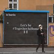 TOPSHOT - A man wearing a face cover waits for the light to change in front of a poster reading: "Let's be together at home" in Berlin on April 10, 2020 amid the novel coronavirus pandemic. (Photo by John MACDOUGALL / AFP)