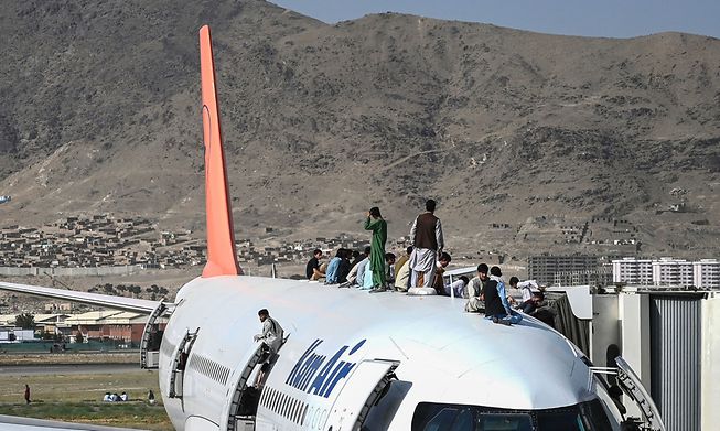 Afghan people climb atop a plane as they wait at the Kabul airport in Kabul on August 16