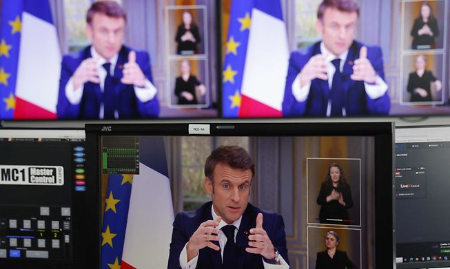 French President Emmanuel Macron is seen on screens as he speaks during a TV interview from the Elysee Palace, in Paris, on 22 March, 2023