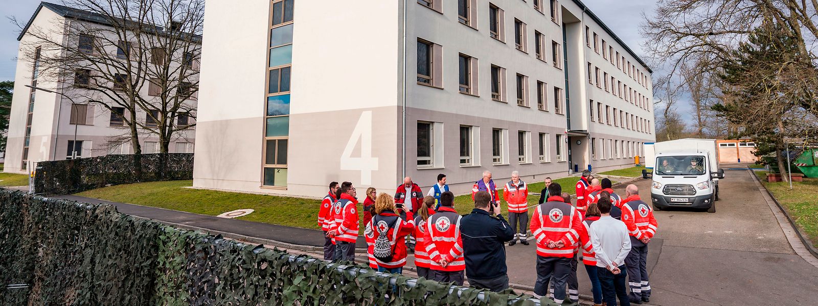 Mitarbeiter des Roten Kreuzes stehen auf dem Gelände der Kaserne Südpfalz der Bundeswehr vor dem Gebäude.