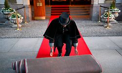PRODUKTION - 16.03.2023, Berlin: Doorman Timothy Uhunamure rollt vor dem Hotel Adlon den roten Teppich aus. Zu manchen Details eines königlichen Besuchs wird traditionell geschwiegen. Insidern zufolge wird König Charles III. wohl dort unterkommen, wo bereits seine Mutter Queen Elizabeth II. zu Gast war. Eine der drei Präsidenten-Suiten wurde im Hotel Adlon ihr zu Ehren zur Royal Suite ernannt. Foto: Jens Kalaene/dpa +++ dpa-Bildfunk +++