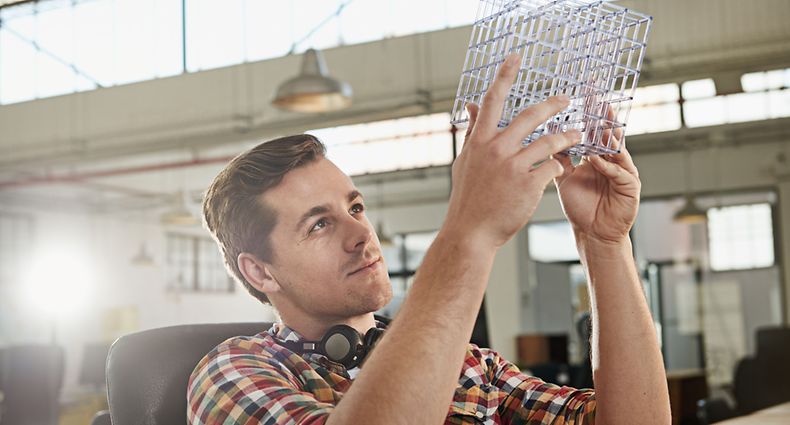 Shot of a young male designer looking thoughtfully at the cube model he's holding