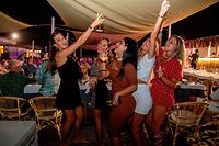 Women dance on the sand at an outdoor restaurant of a beach in Fregene near Rome, on August 14, 2020. - "Put your masks on!" repeats the DJ, shouting vainly into his microphone, but the  dancers below, dripping in sweat, don't seem to care. While the threat of a second wave of coronavirus looms nearer in several European countries, such as Spain, Italy is trying to stem new infections in the middle of "Ferragosto", the sacrosanct holiday weekend of August 15. (Photo by Tiziana FABI / AFP)