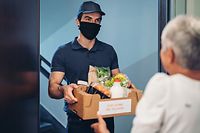 Young man with a face mask delivering groceries during the pandemic