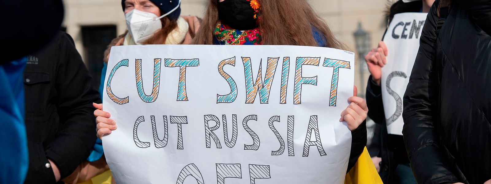 Berlin: Teilnehmer an einer Solidaritäts-Demonstration für die Ukraine stehen auf dem Pariser Platz mit einem Plakat "Cut Swift Cut Russia Off".