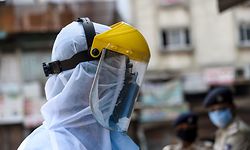 A health worker wearing protective gear walks past police personnel (background) during a screening and checking session at a residential area during a government-imposed nationwide lockdown as a preventive measure against the COVID-19 coronavirus, in Ahmedabad on April 9, 2020. (Photo by SAM PANTHAKY / AFP)