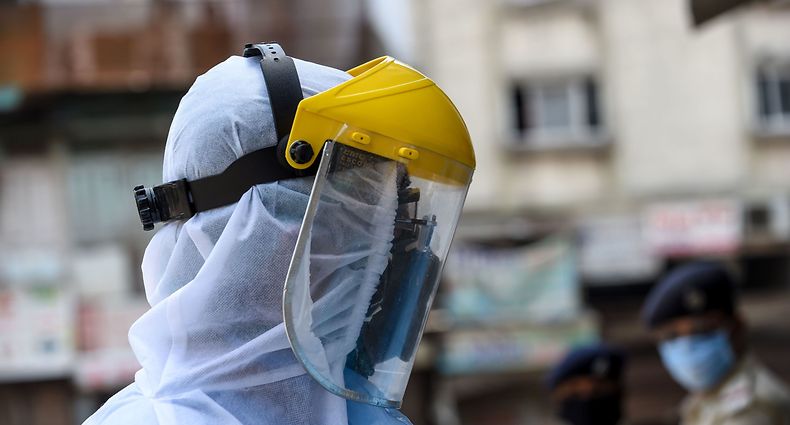 A health worker wearing protective gear walks past police personnel (background) during a screening and checking session at a residential area during a government-imposed nationwide lockdown as a preventive measure against the COVID-19 coronavirus, in Ahmedabad on April 9, 2020. (Photo by SAM PANTHAKY / AFP)