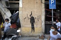 Members of the Lebanese civil society carrying brooms used for clearing debris, walk past a wall painting depicting a hanged politician and reading (death sentence in Arabic) in the partially damaged Beirut neighbourhood of Mar Mikhael on August 7, 2020. (Photo by PATRICK BAZ / AFP)