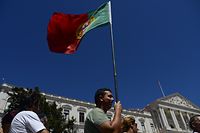 A demonstrator holds the Portuguese flag in front of the Portuguese parliament as he participates with hundreds of others in a demonstration called by the main Portuguese union CGTP-IN (General Confederation of the Portuguese Workers) to protest against anti-labor and anti-social policies of the Portuguese government in Lisbon on July 22, 2015.   AFP PHOTO/ PATRICIA DE MELO MOREIRA
