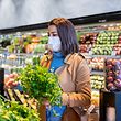 Woman wearing protective face mask buying vegetables in supermarket in the new normal