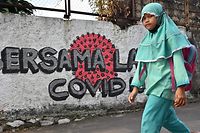 "Zusammen gegen Covid-19" steht auf der Mauer, an der ein Mädchen in Jakarta vorbeigeht.