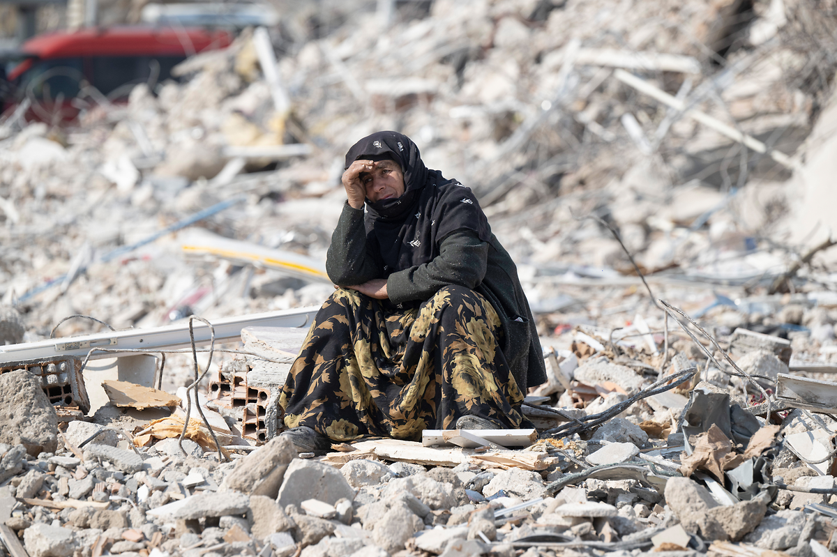 Eine Frau sitzt zwischen den Trümmern und beobachtet die Bergung von Opfern im türkischen Antakya. 