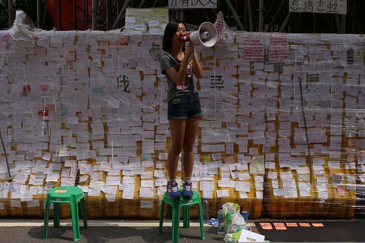 A student protester speaks into a microphone in front of a "democracy wall" filled with notes supporting the pro-democracy protest in Hong Kong on October 2, 2014. Tensions in Hong Kong soared after police were seen unloading boxes of tear gas and rubber bullets close to the city's besieged government headquarters as the authorities urged pro-democracy demonstrators to disperse "as soon as possible". AFP PHOTO / AARON TAM