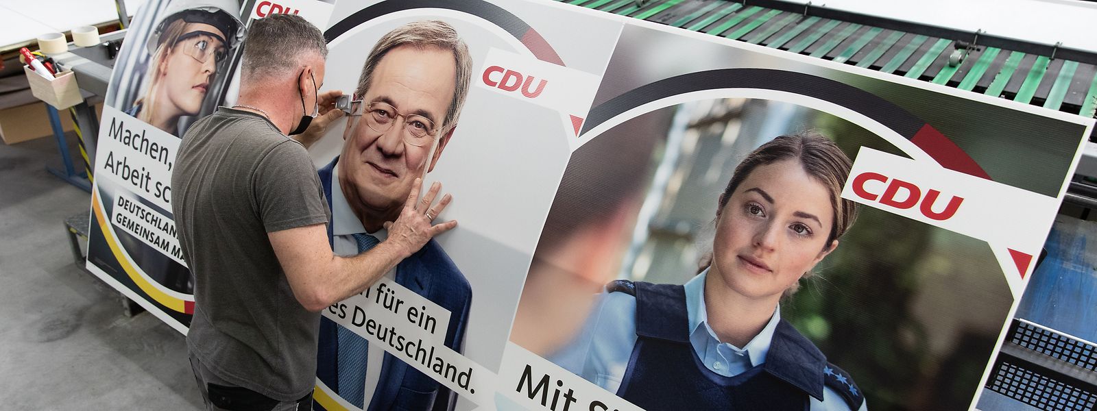 Drucker Marc Berenbrinker kontrolliert mit einer Lupe ein Wahlplakat der CDU mit einem Bild des Bundeskanzlerkandidaten Armin Laschet darauf.