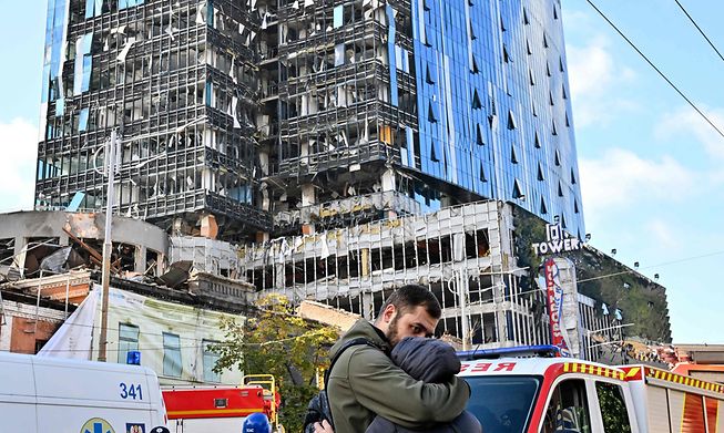 People react outside a partially destroyed multistorey office building after several Russian strikes hit the Ukrainian capital of Kyiv on October 10, 2022, amid Russia's invasion of Ukraine. 