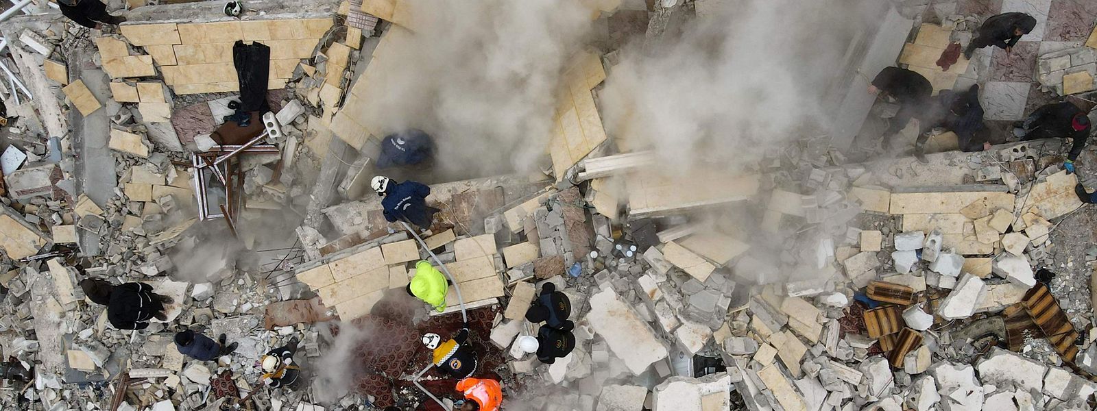 Eine Luftaufnahme zeigt Anwohner, die im syrischen Sarmada mithilfe von Bulldozern nach Opfern und Überlebenden in den Trümmern eingestürzter Gebäude suchen.