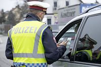 An Austrian police officer checks a driver's vaccination certificate on a smartphone during a traffic control in Graz, Austria, on November 15, 2021, during the ongoing coronavirus (Covid-19) pandemic. - Austria became the first EU country on November 15 to impose a lockdown on the unvaccinated and began inoculating children as young as five as the virus strengthens its grip on the continent. Unvaccinated people in Austria are only allowed to leave their homes for very specific reasons. They are still allowed to go to work, but there the 3G rule (vaccinated, recovered or tested) applies without exception. (Photo by ERWIN SCHERIAU / APA / AFP) / Austria OUT