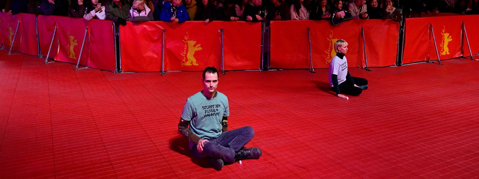 Aktivisten der Umweltgruppe „Letzte Generation“ kleben mit einem T-Shirt mit der Aufschrift „Stoppt den Wahnsinn der fossilen Brennstoffe“ auf dem Boden in der Nähe des roten Teppichs zum Auftakt der Berlinale.