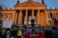 A protester stands wrapped in black-white-red imperial German flag in front of the Reichstag building guarded by policemen at the end of a demonstration called by far-right and COVID-19 deniers to protest against restrictions related to the new coronavirus pandemic, in Berlin, on August 29, 2020. - At the start of August, a similar "anti-corona" march in Berlin took place with 20,000 protesters, a mixture of the hard left and right, anti-vaccination campaigners, conspiracy theorists and self-described "free thinkers". Police broke up the protest early after participants repeatedly flouted Covid-19 safety regulations. (Photo by John MACDOUGALL / AFP)