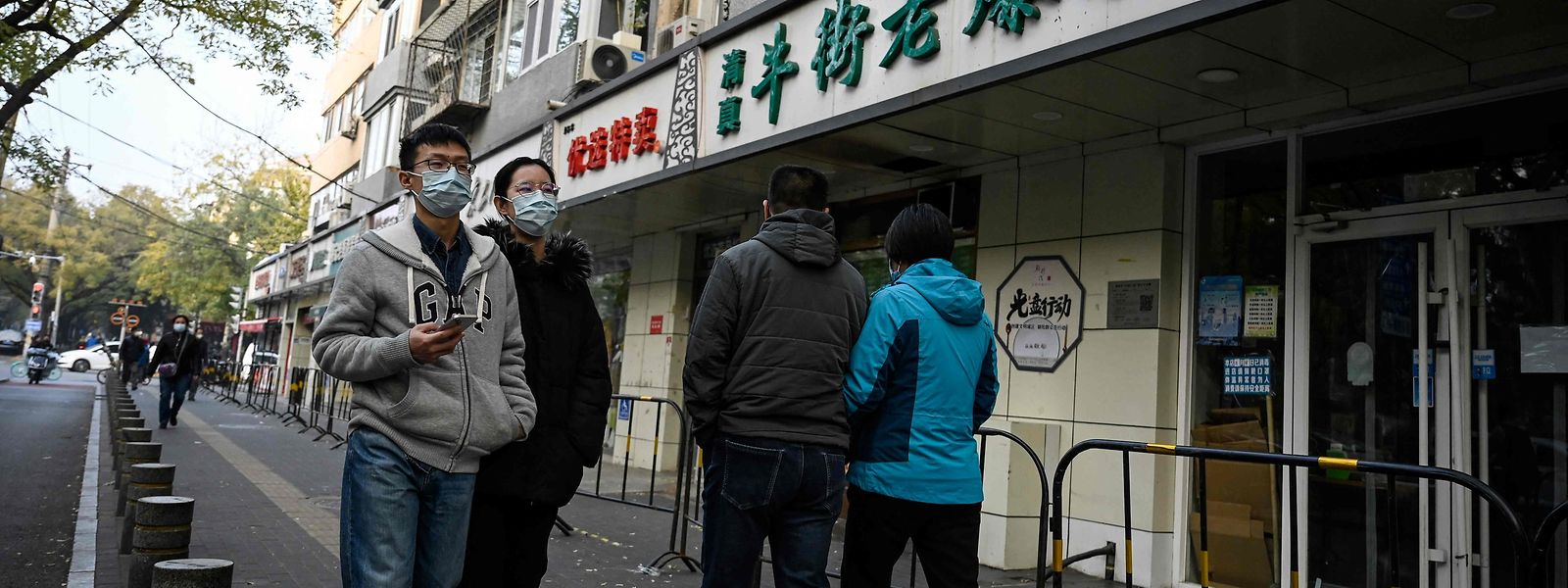 Menschen in Peking passieren vor geschlossenen Läden.